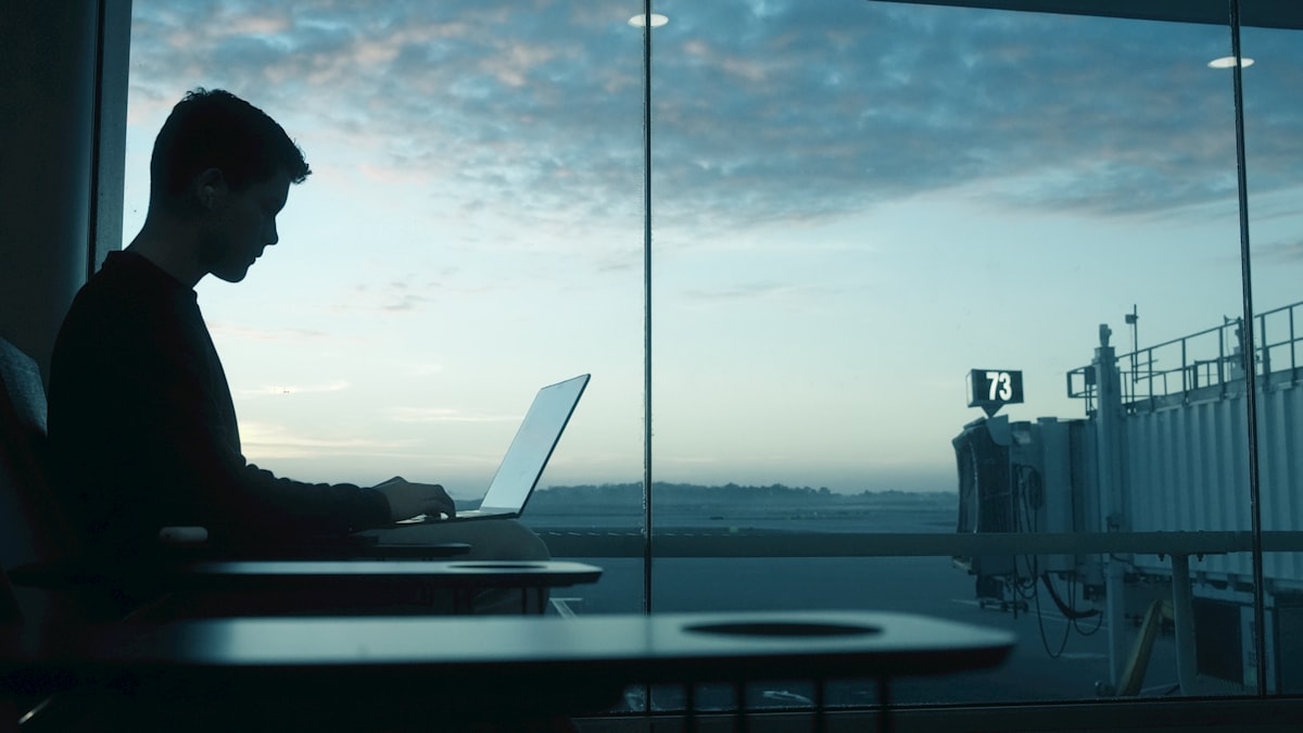 Best Laptops for Business Travel in 2026 Man working on laptop by an airport window at sunrise
